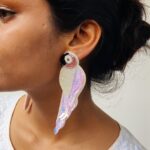 Close-up of handcrafted pearly pink parrot earrings with iridescent beadwork placed on a champagne satin background.
