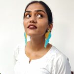 Indian woman wearing a pair of handcrafted teal-blue and golden parrot earrings, styled in a white kurta and looking upwards with a playful expression.