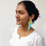 Teal blue and golden beaded handcrafted parrot-shaped statement earrings worn by a woman in white ethnic attire.