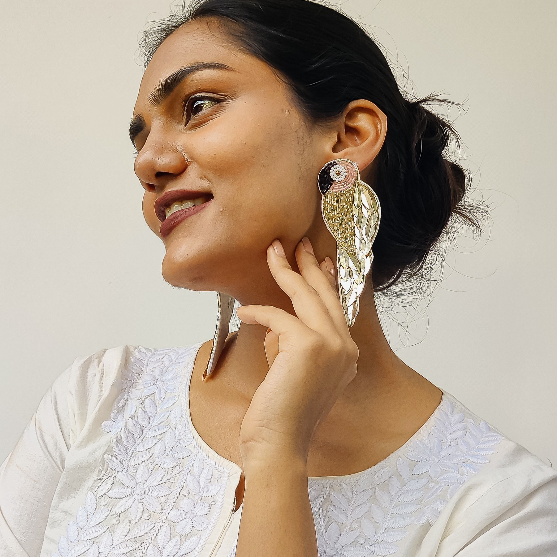 Golden Parrot Earrings – Close-Up Lifestyle Shot | Masaira Designer Jewellery Model in white chikankari kurta smiling with hand near ear, showcasing Masaira’s golden parrot earrings with sequin and pearl detailing