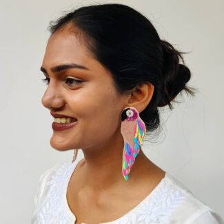Model smiling in profile wearing tropical multicolour parrot earrings with pearl eyes and rainbow sequin feathers — Masaira festive collection