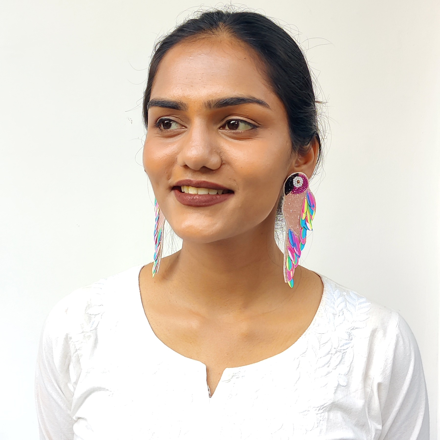 Front-facing image of model wearing colourful handcrafted parrot earrings with sequin feather detailing — Masaira festive accessories