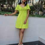 : Full-length image of woman wearing Masaira’s parrot earrings with green mini dress and white heels.