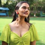 Indian model smiling and looking upward while wearing tropical toucan earrings, outdoors in natural sunlight with green background.