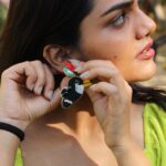 Woman holding toucan-inspired earring close to her ear, showcasing red flower and black-beaded bird design.