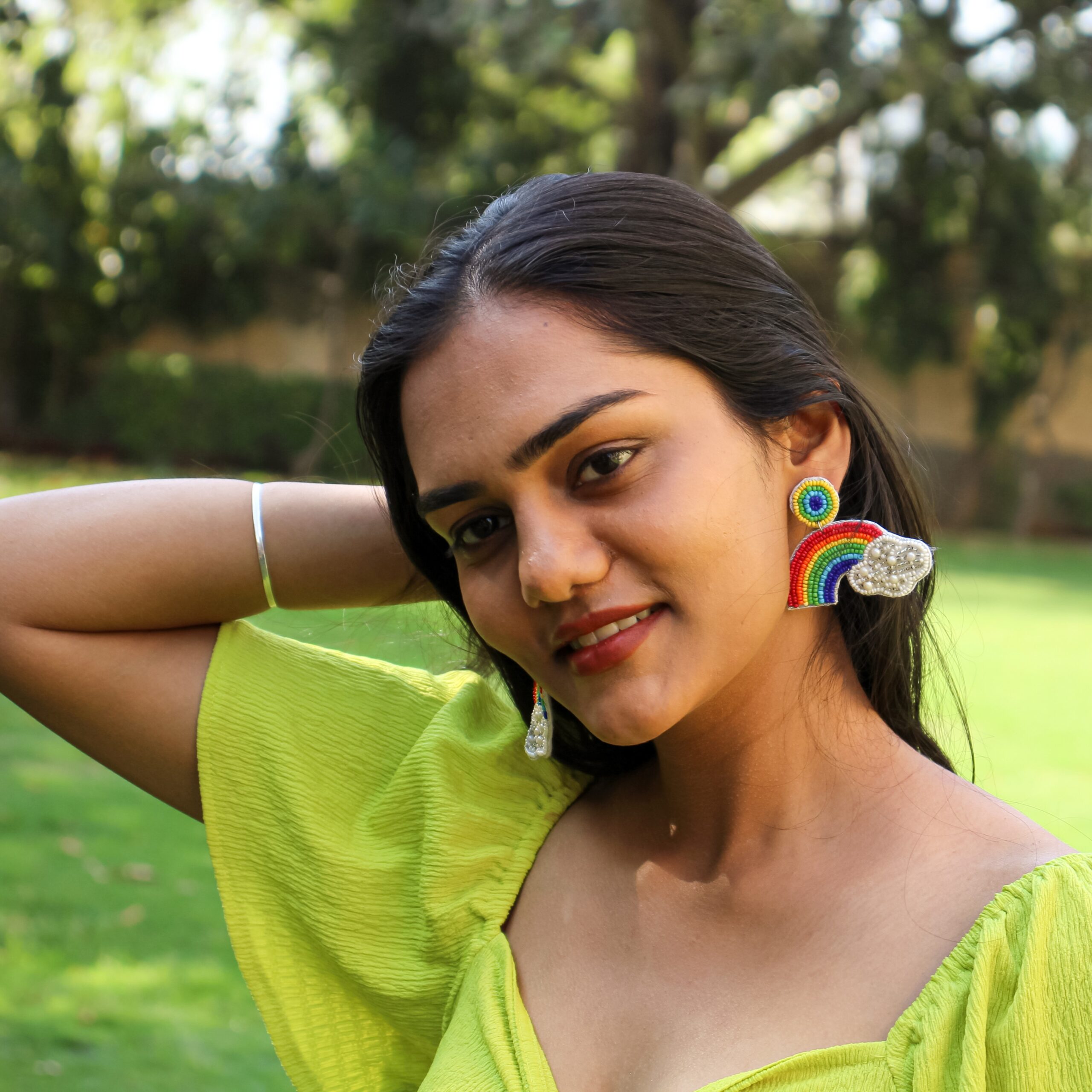 Close-up of handcrafted rainbow beaded earrings with cloud design, worn by a smiling woman.