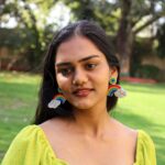 Smiling woman outdoors wearing rainbow beaded earrings with pearl clouds, styled with a green dress Title: