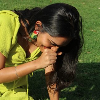 Laughing Indian woman wearing Masaira’s Shimmering Lovebirds statement earrings while sitting outdoors on grass