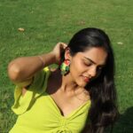 Indian woman wearing handcrafted Shimmering Lovebirds beaded earrings with hand behind her ear, sitting on green grass