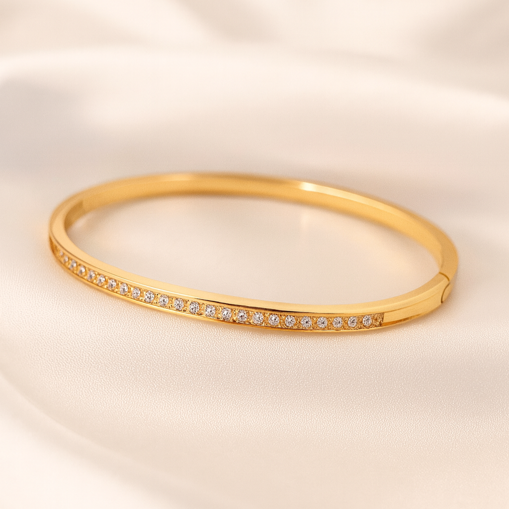 lustre-line-bangle-gold-plated-zircon-masaira Slim gold-plated bangle with white cubic zirconia stones from Masaira on a satin background