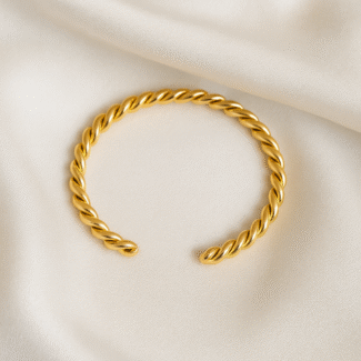 Gold-plated twisted torque cuff bracelet in open design on satin background by Masaira