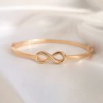 Gold-plated infinity symbol bangle bracelet on soft white satin background by Masaira