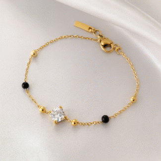 Gold-plated mangalsutra bracelet with a solitaire cubic zirconia center and black beads on satin background by Masaira