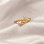 Gold open ring with a pink heart-shaped stone placed on ivory satin fabric