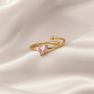Gold open ring with a pink heart-shaped stone placed on ivory satin fabric