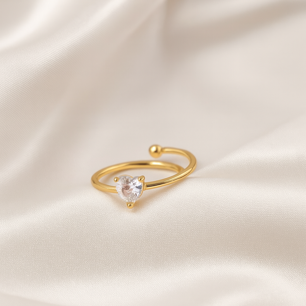 Gold open ring with a heart-cut clear stone placed on white satin fabric