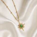 18 carat gold plated sunburst necklace with green stone pendant on satin background