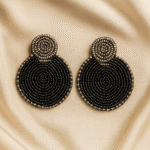 Handcrafted black and gold circular beaded earrings on a champagne satin background