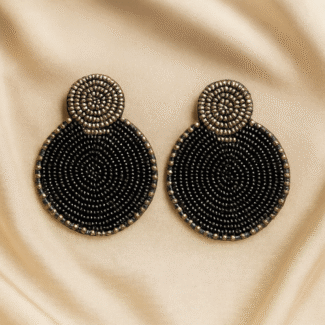 Handcrafted black and gold circular beaded earrings on a champagne satin background