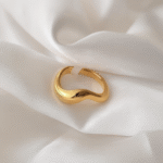 Gold sculptural wave ring placed on ivory satin fabric
