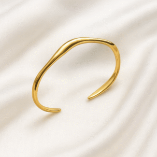 Gold-plated wavy open cuff bangle placed on ivory satin background