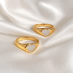 Two gold signet rings with white heart inlays placed on a white ceramic dish
