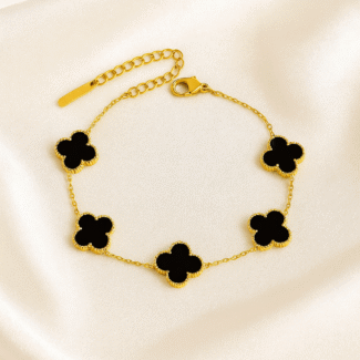 Gold-plated bracelet with black clover charms laid on ivory satin background by Masaira