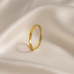 Slim gold band ring with micro-set clear stones photographed against soft stone background