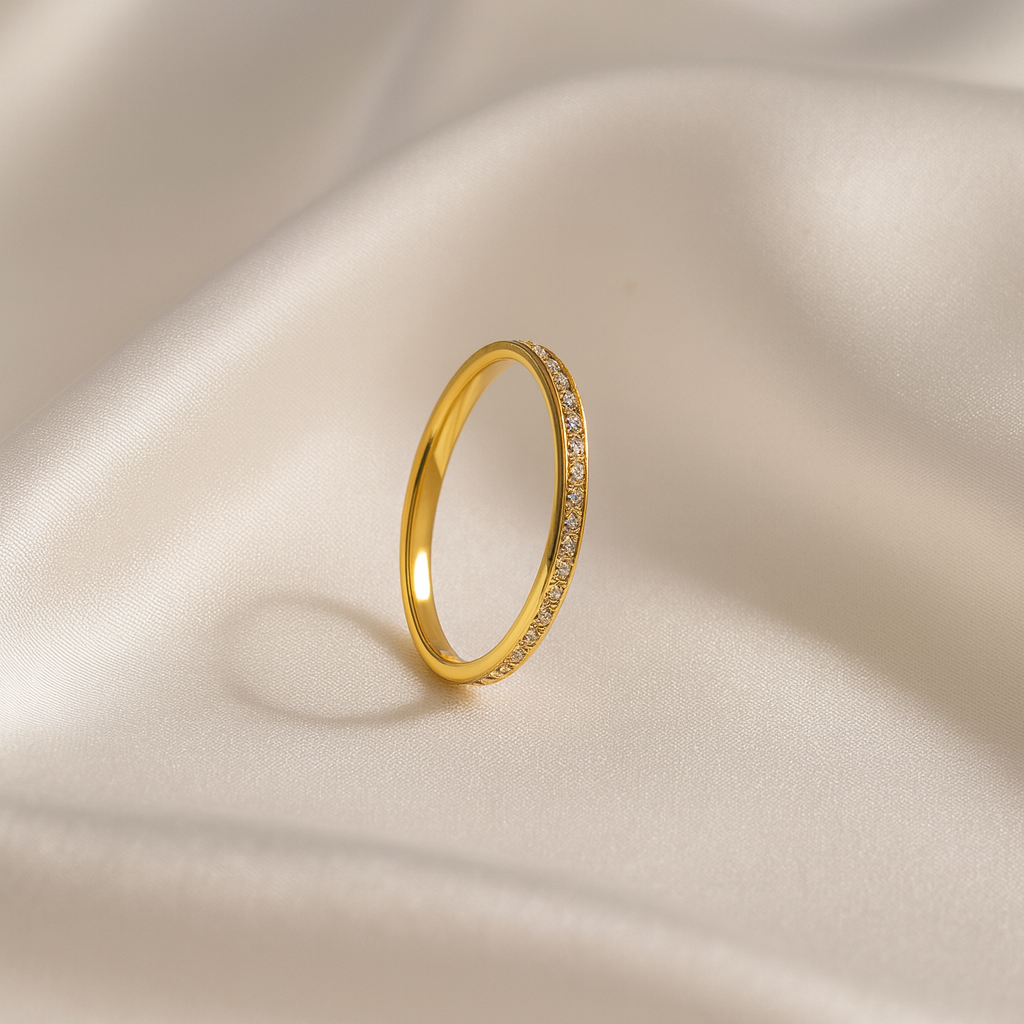 Slim gold band ring with micro-set clear stones photographed against soft stone background