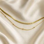 18 carat gold plated dual-layer necklace with snake chain and beaded chain on satin background