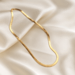 Flat gold snake chain necklace with 18 carat gold plating displayed on ivory satin fabric