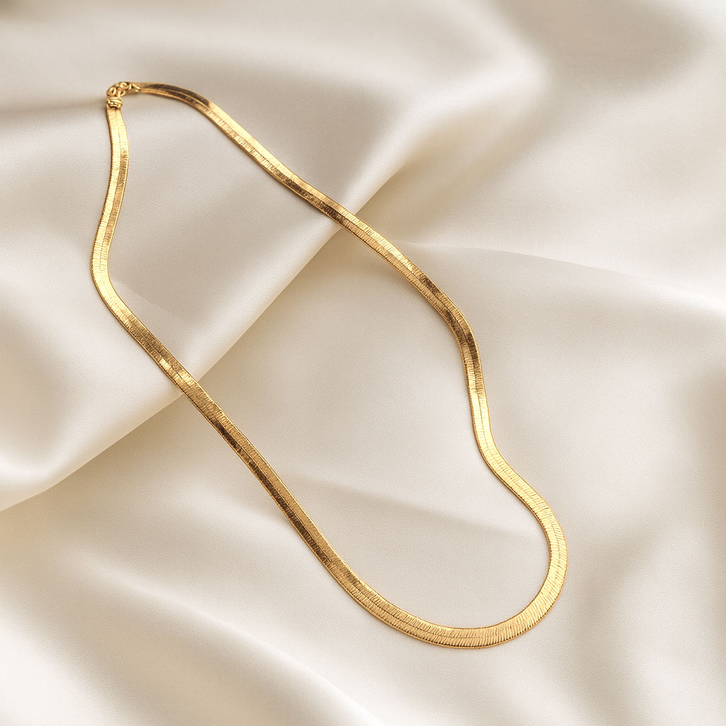 Flat gold snake chain necklace with 18 carat gold plating displayed on ivory satin fabric