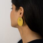 Side profile of a woman wearing a round matte gold statement earring with a modern vertical slit.