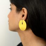 Close-up of a woman wearing a minimalist brushed gold disc earring with a narrow top slit.