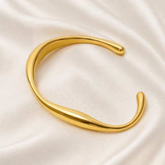Open sculptural gold bangle with curved edges on satin background