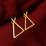 Minimalist triangle gold-plated earrings with modern geometric design placed on a maroon satin background.