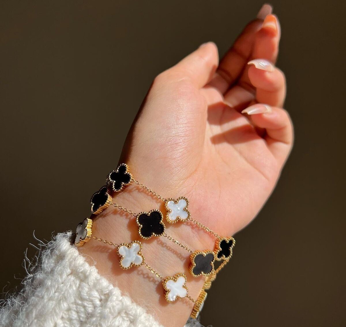 Stacked Clover Bracelets – Gold-Plated Black & White Floral Charm Bracelets by Masaira Woman wearing stacked gold-plated black and white clover charm bracelets on wrist in natural daylight
