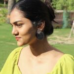 Smiling woman outdoors wearing black and gold handcrafted circular earrings, styled with a lime green top.