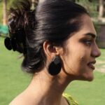 Woman wearing handcrafted black and gold circular earrings in outdoor garden setting