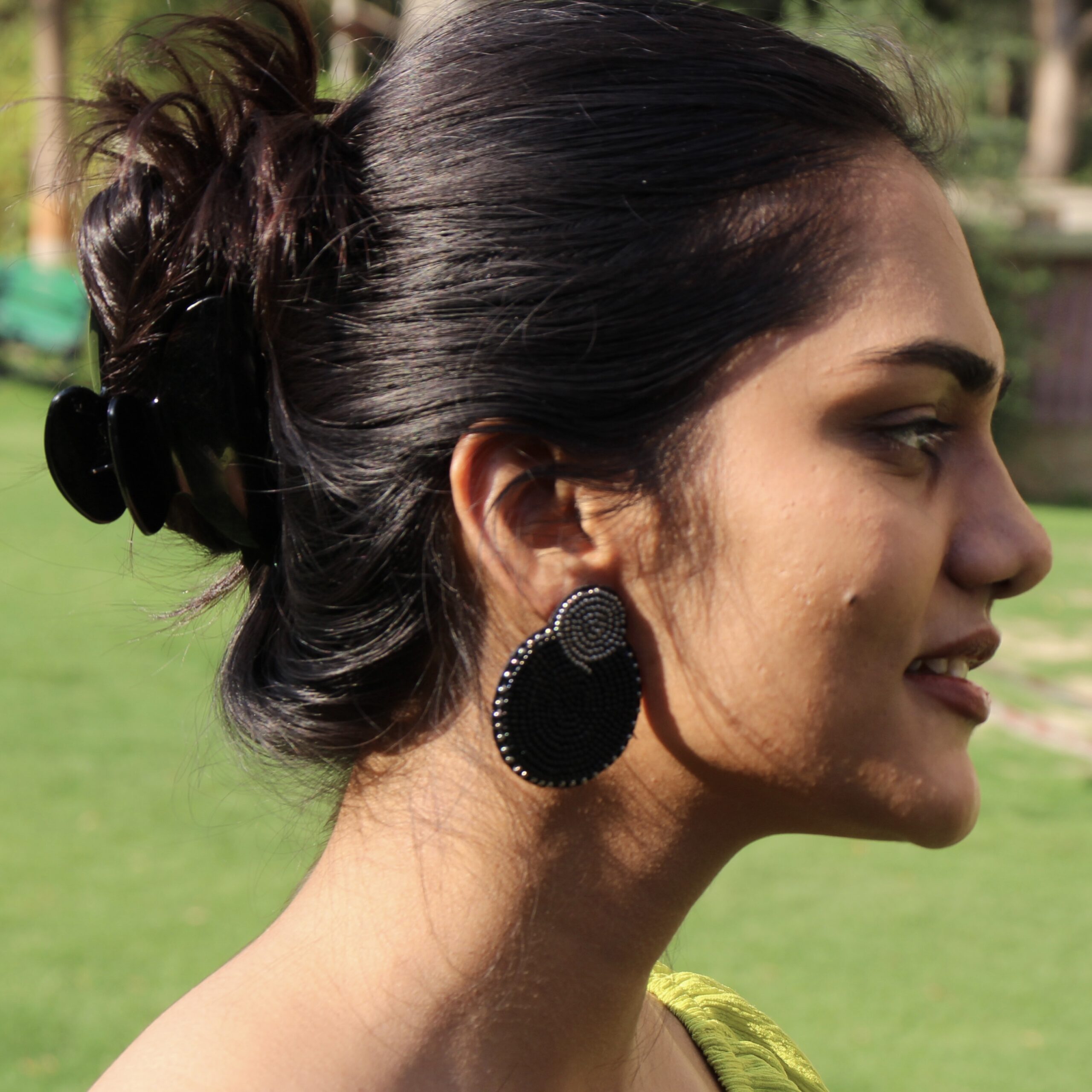 Elegant Side Profile with Midnight Muse Earrings Woman wearing handcrafted black and gold circular earrings in outdoor garden setting