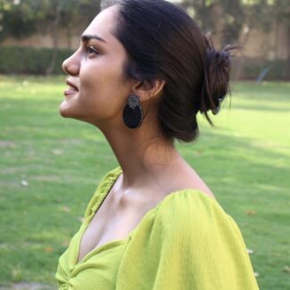 Model in lime green dress wearing black and gold beaded earrings in garden backdrop