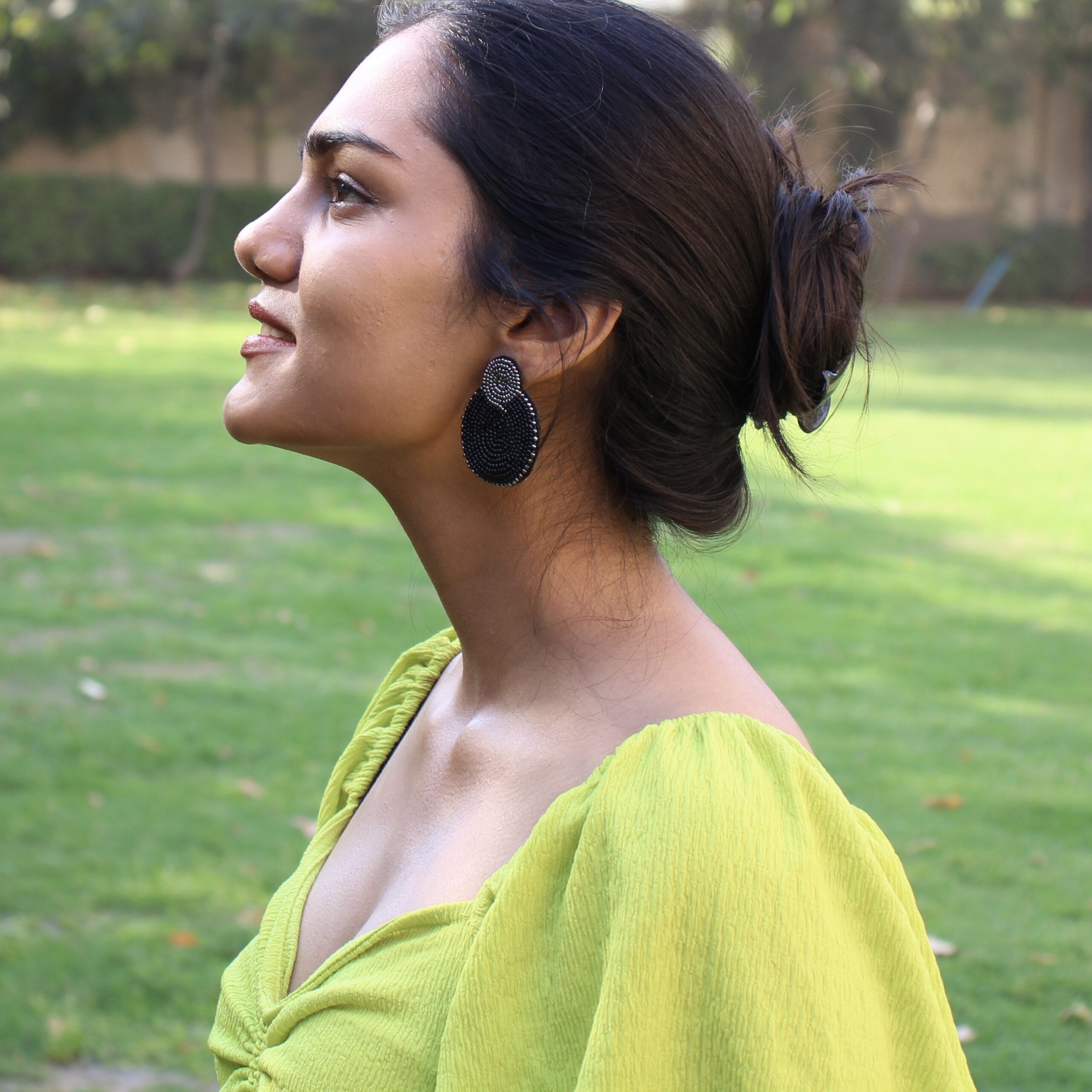Outdoor Glamour in Midnight Muse Earrings Model in lime green dress wearing black and gold beaded earrings in garden backdrop