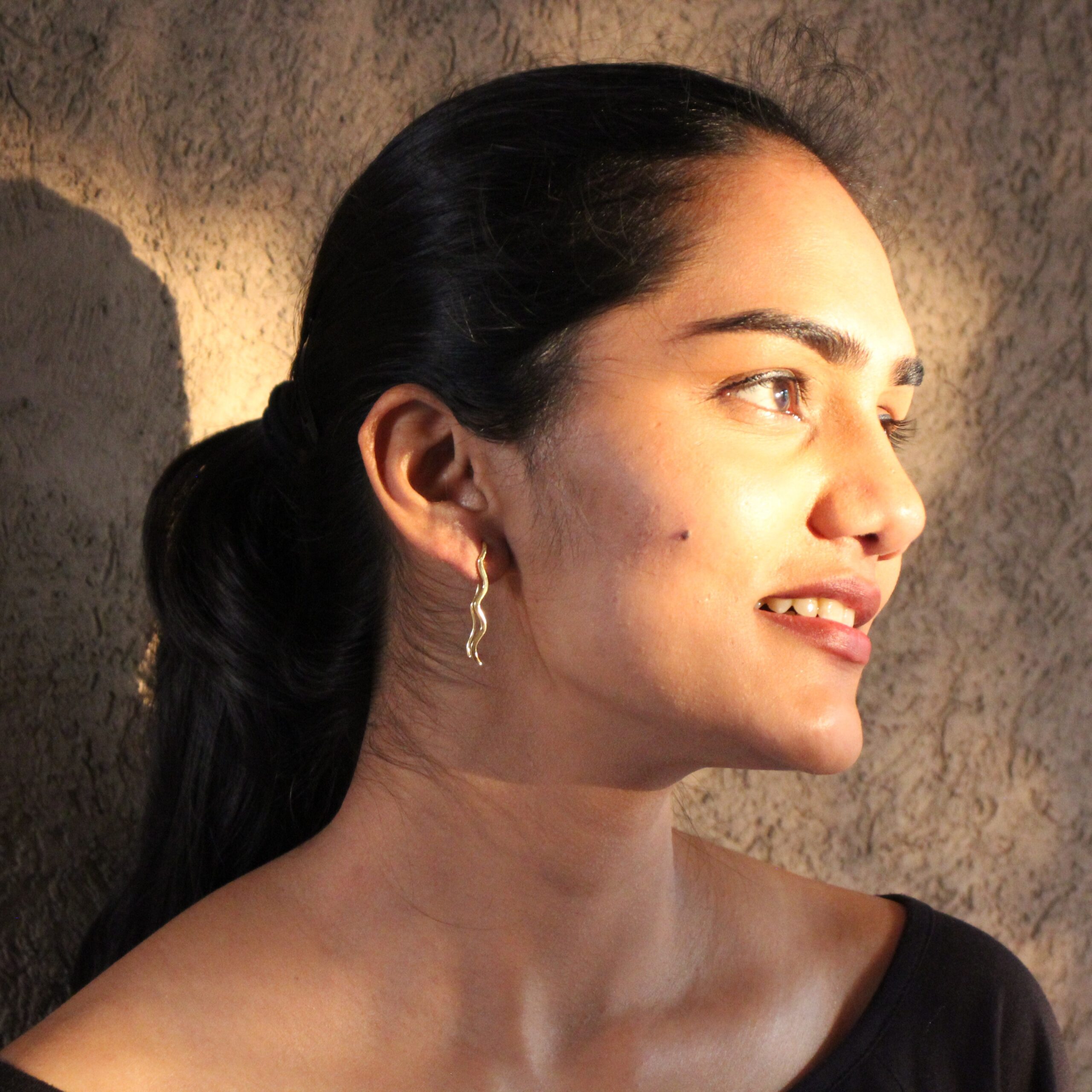 Minimalist gold-plated wavy earrings on woman with ponytail, lightweight modern design