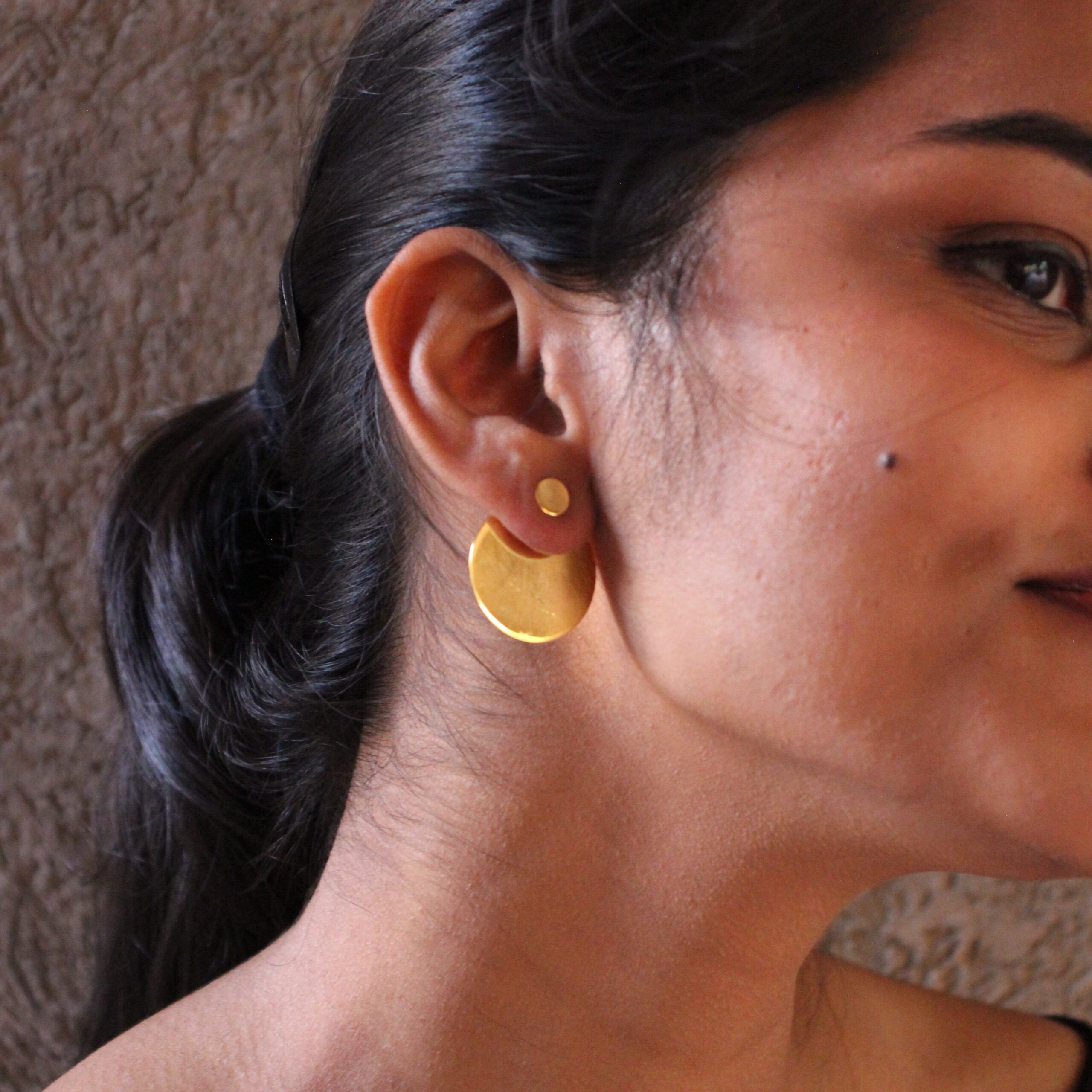 Close-up of gold-plated circular stud earrings with textured finish