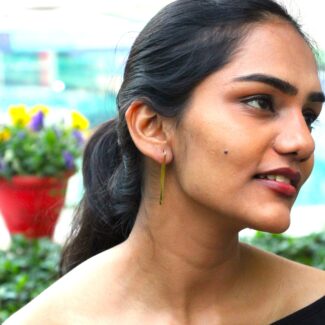 Minimalist long gold-plated drop earrings worn by a woman with tied hair, styled outdoors against a natural background.