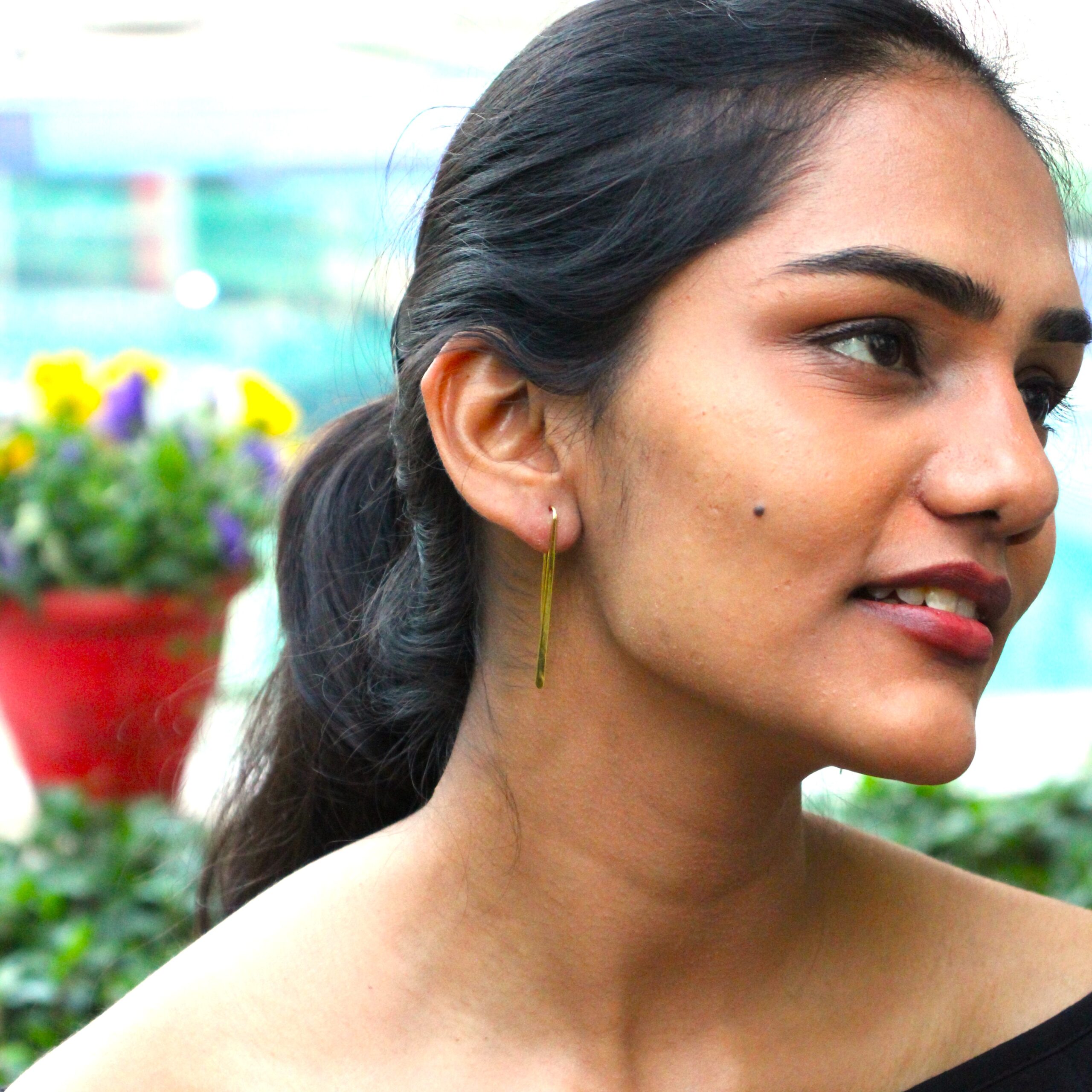 Minimalist long gold-plated drop earrings worn by a woman with tied hair, styled outdoors against a natural background.