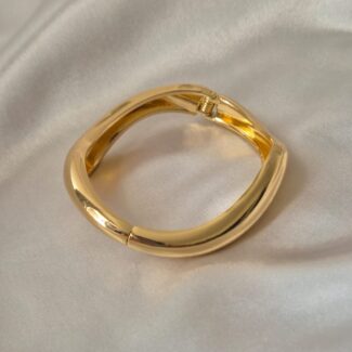 Polished gold-plated bold square bangle with hinge clasp on satin background by Masaira