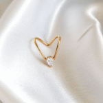Heart-shaped open gold ring with a clear round stone placed on satin white background