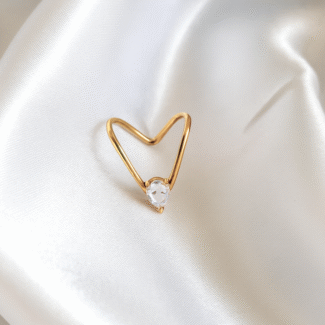 Heart-shaped open gold ring with a clear round stone placed on satin white background