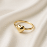 Gold band ring with a polished heart centerpiece placed on a textured ivory surface